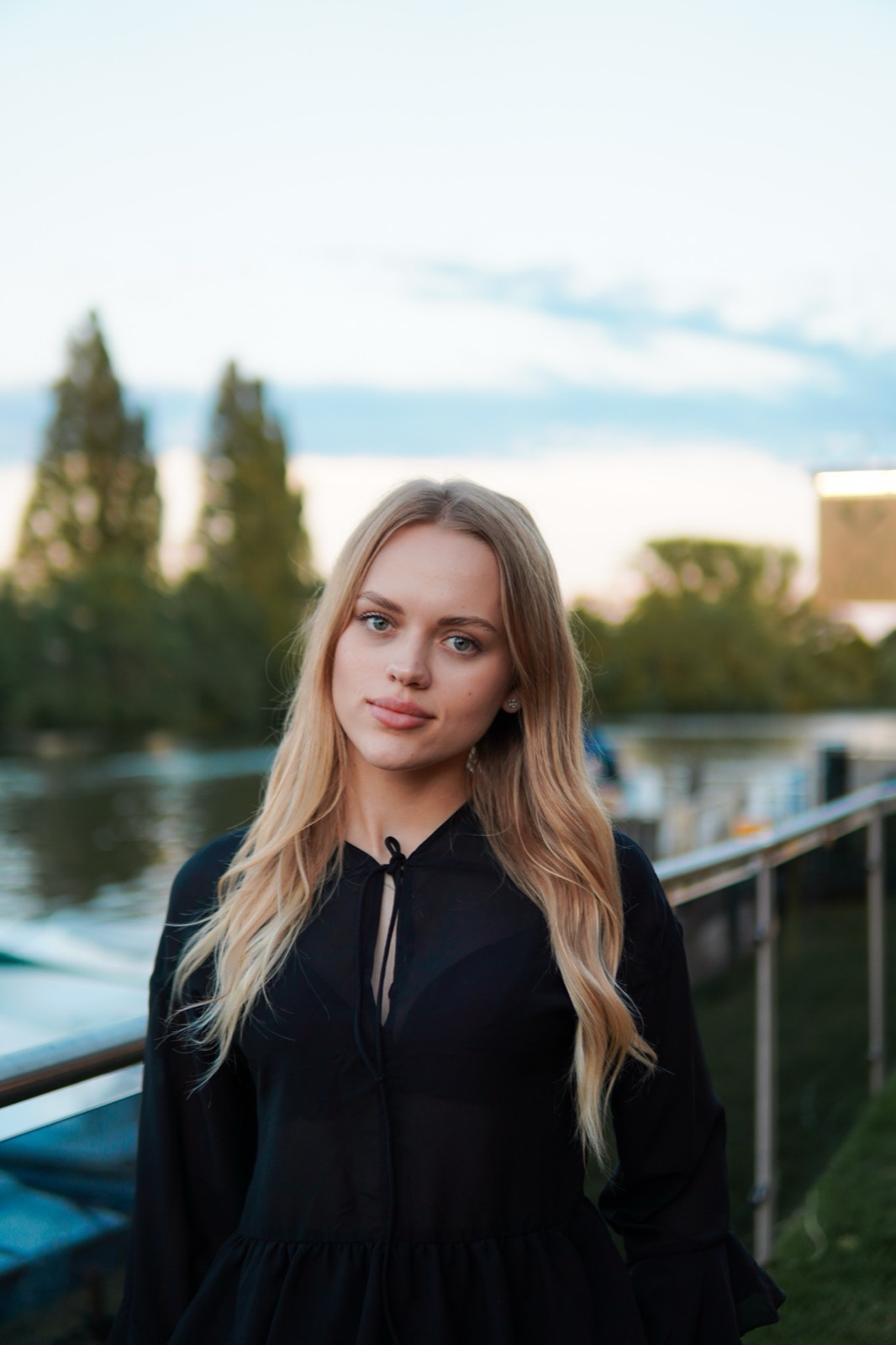 Portrait of a blonde woman in black by the river at dusk