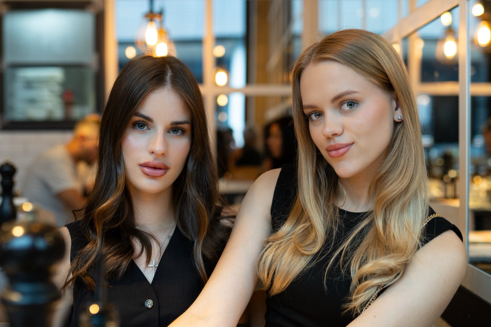 Two women in black dresses at a softly lit café